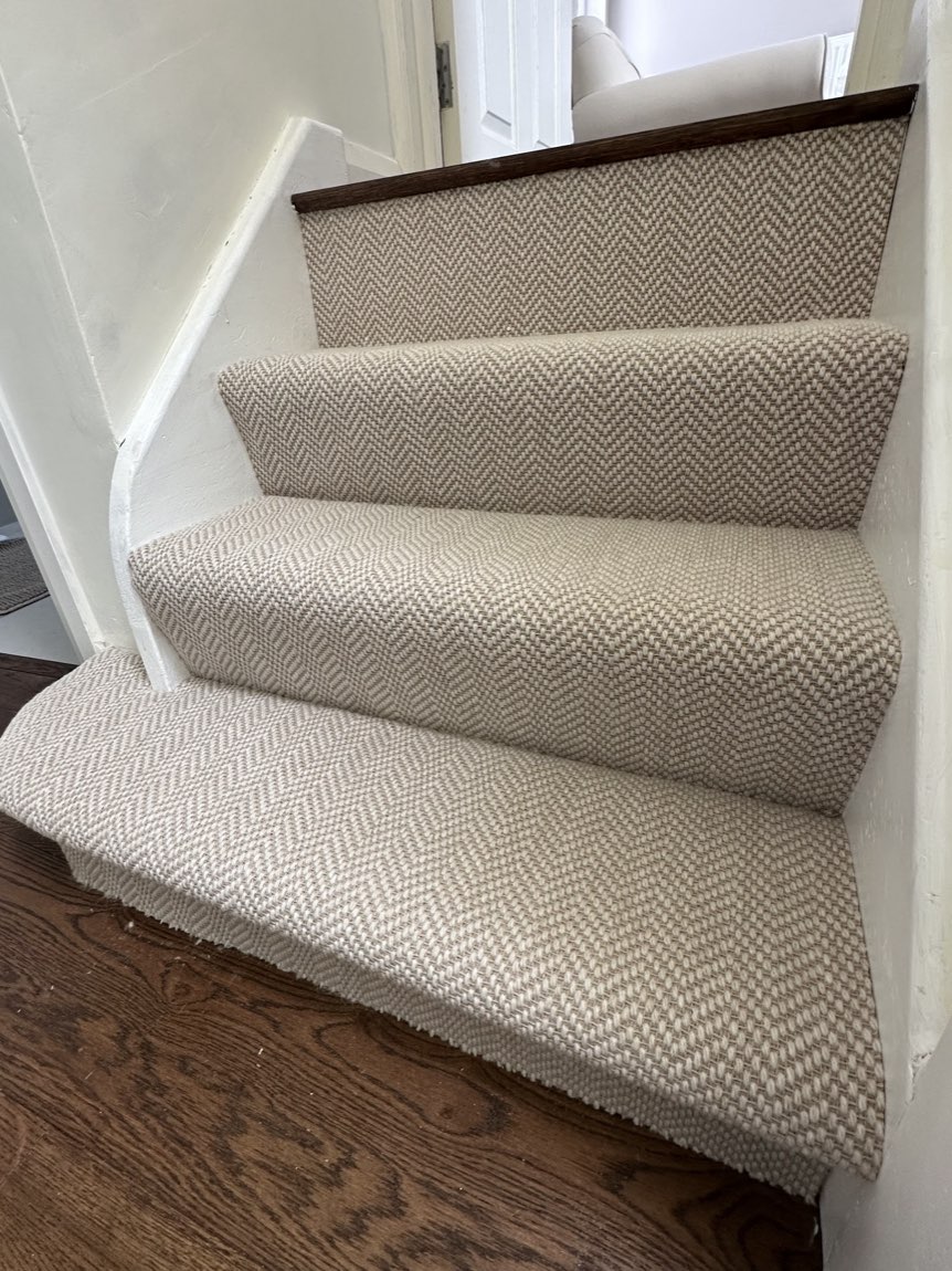 A beige herringbone-weave stair runner fitted down a curved staircase onto a dark oak floor.