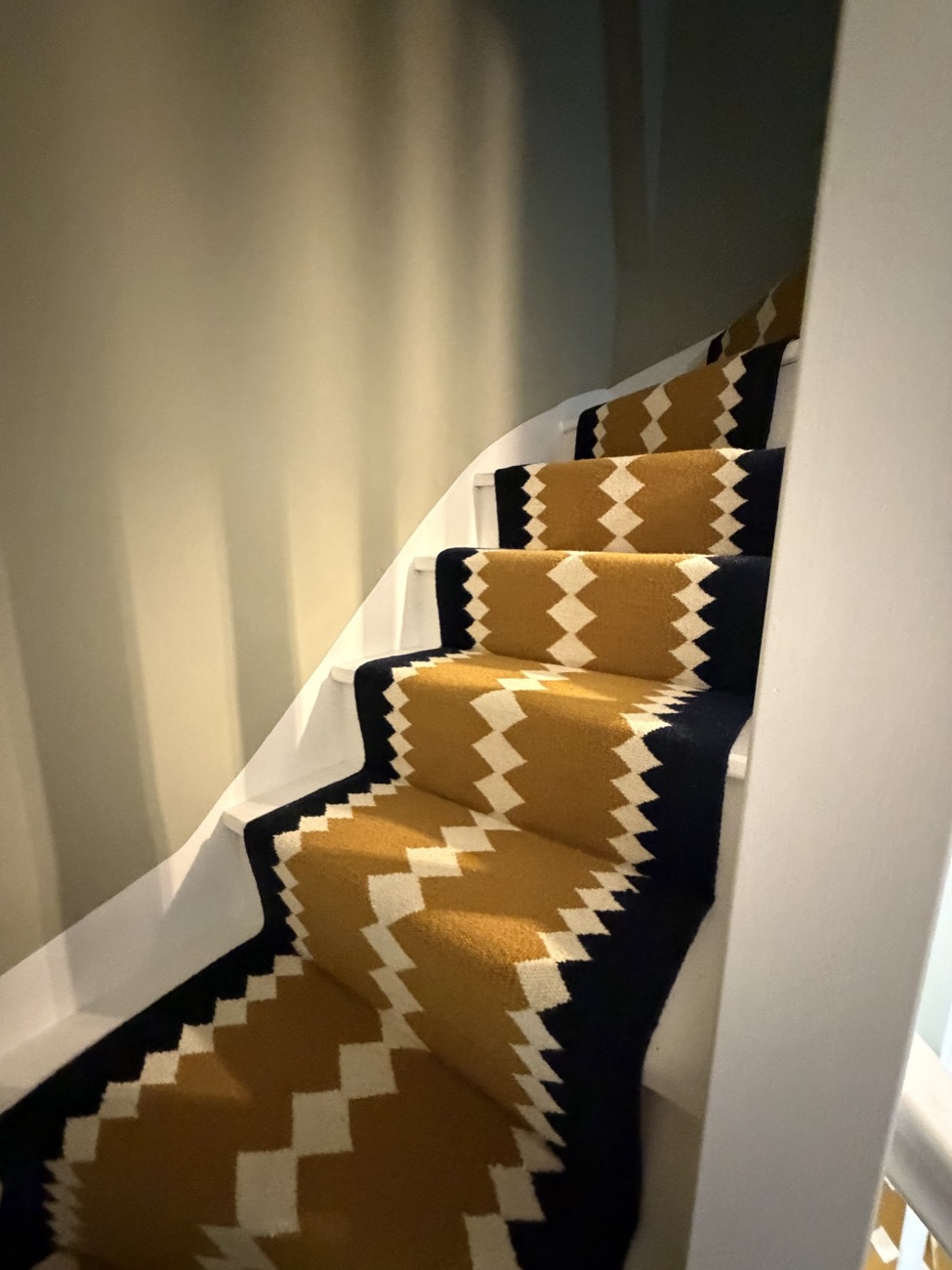 A mustard and navy zigzag stair runner lit warmly as it winds up a white staircase.