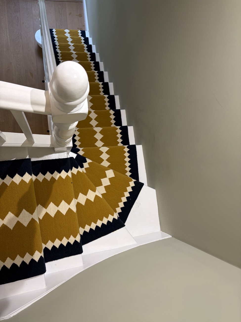 A mustard, navy and cream zigzag stair runner viewed from the top of the stairs, fitted crisply around the turn.