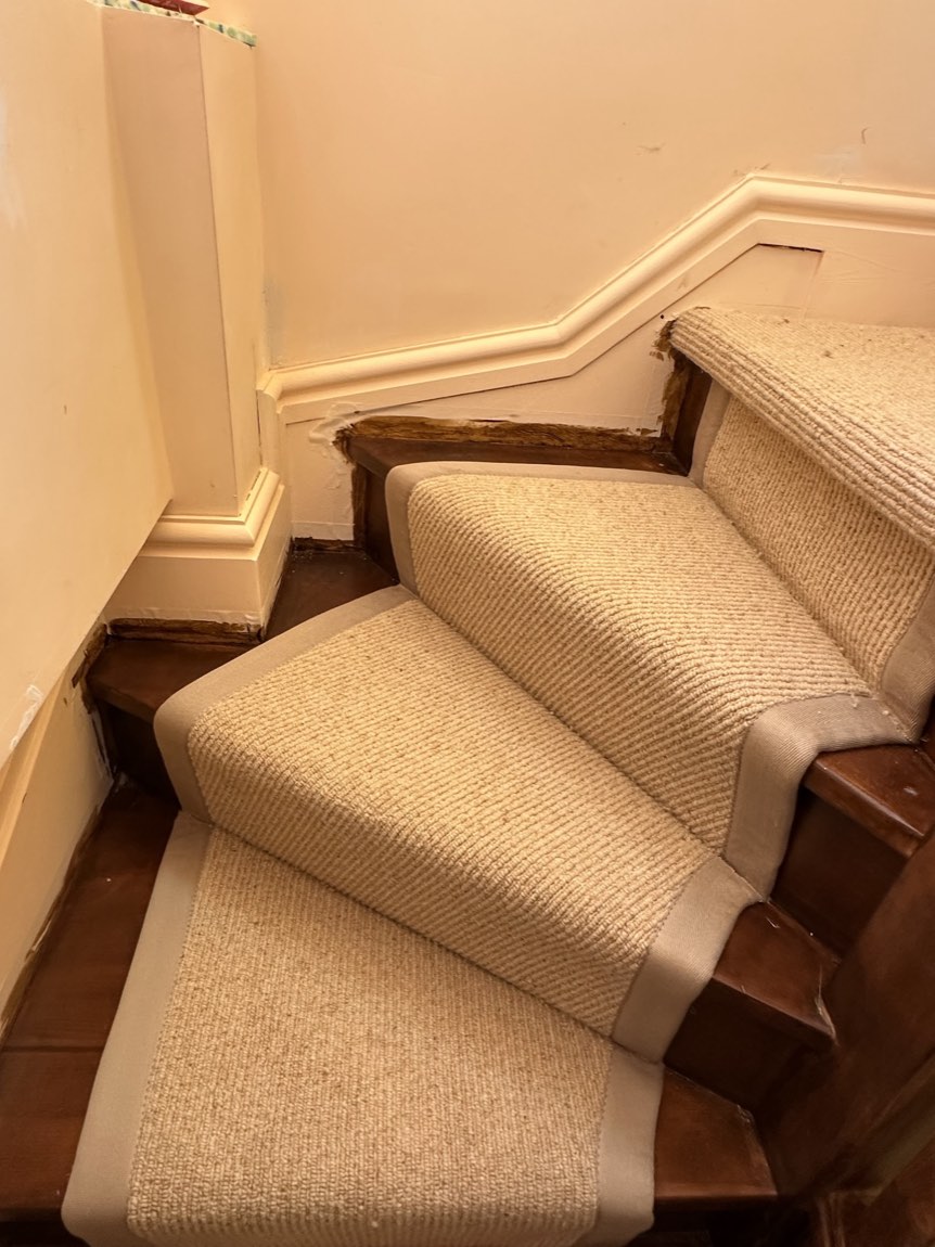 A natural sisal-look stair runner with a bound border being fitted onto dark timber stairs.