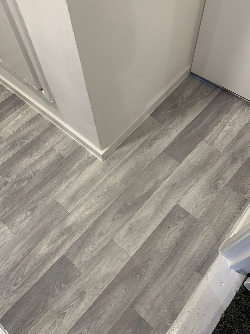 Grey wood-effect vinyl plank flooring laid neatly around a doorway and skirting.